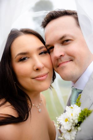 Close-up wedding portrait showing tender moment between newlyweds with white floral bouquet.