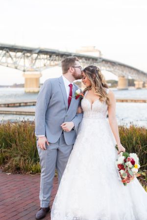 A romantic wedding portrait by a bridge with a couple in grey suit and white lace gown holding a bouquet.