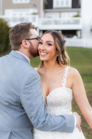 Tender wedding moment captured between newlyweds wearing grey suit and white lace dress.