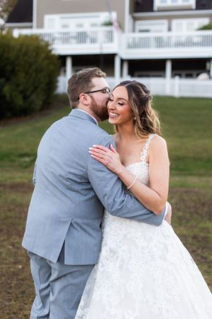 Intimate outdoor wedding photo showing couple embracing in grey suit and white gown.