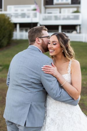 A romantic moment between newlyweds in a lace dress and grey suit outdoors.