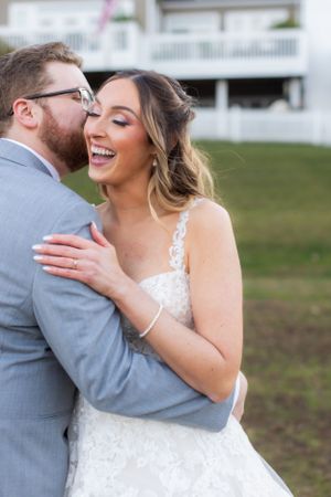 A joyful candid moment between newlyweds in grey suit and lace dress outdoors.