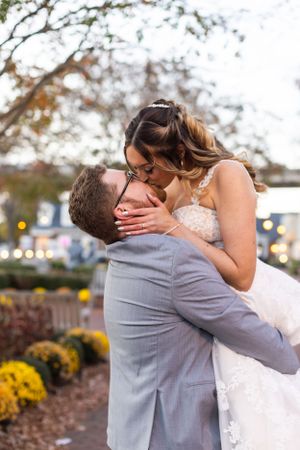 A romantic kiss between newlyweds surrounded by autumn foliage and yellow mums.