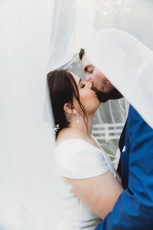 A romantic wedding kiss captured through flowing white veil fabric.