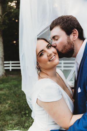 A tender wedding moment as groom kisses bride under flowing white veil.