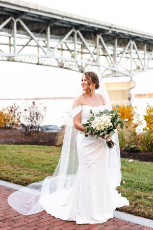 A bride in a flowing white wedding dress sits gracefully on brick steps during an outdoor photoshoot.