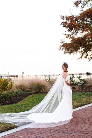A flowing cathedral length veil trails behind a white wedding gown on a brick pathway during an autumn sunset.