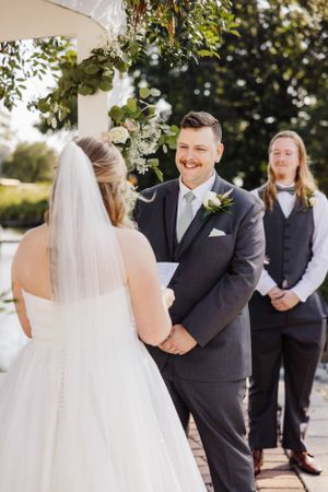 Wedding ceremony under floral arch with officiant in background.