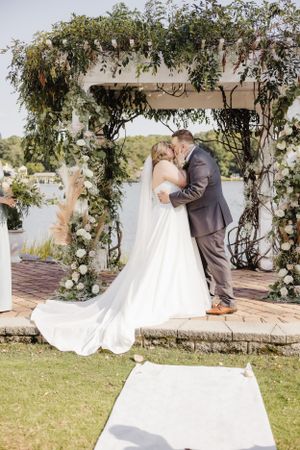 A wedding ceremony kiss under a rustic arch adorned with greenery and flowers.