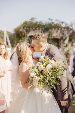 A sunlit wedding ceremony kiss with a lush green and white bouquet.