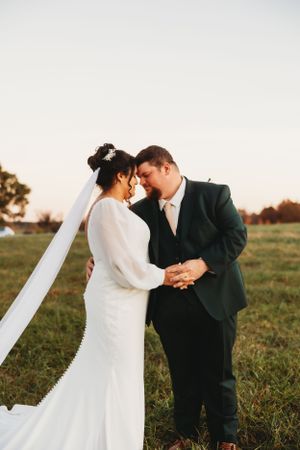 A romantic wedding moment captured in a golden field with a bride in white dress embracing her partner at sunset.