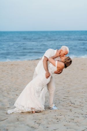 Romantic beach wedding photo with couple in white sharing intimate dance pose.