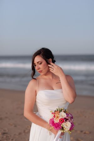Close-up of a bride wearing a strapless gown holding a colorful bouquet on a beach.