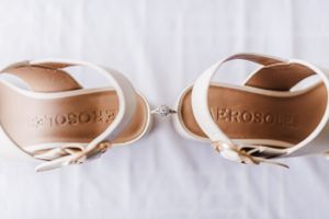 White and tan sandals with 'PRONOVIAS' branding displayed with ring between them.