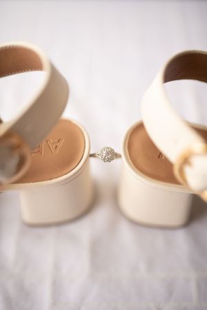 Diamond engagement ring positioned between two cream-colored bridal shoes.