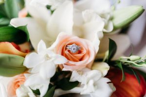 Close-up of diamond ring placed delicately in center of peach rose with white lilies.