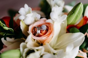 Diamond ring nestled in a peach rose surrounded by white lilies and greenery.