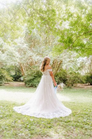 Back view of bride in off-shoulder lace gown with long train standing in garden setting.