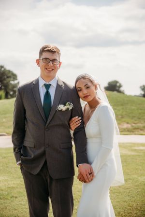 Newlyweds pose together on their wedding day on a grassy hillside.