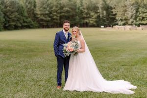A romantic wedding couple poses on a lush green lawn surrounded by trees in the background.