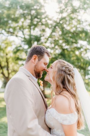 Romantic wedding couple embracing outdoors with groom in tan suit and bride in lace dress.