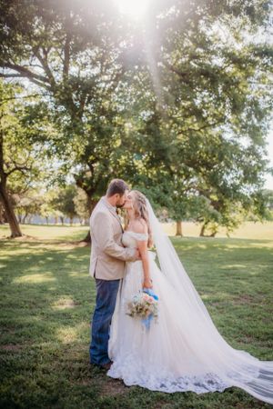 Wedding couple sharing intimate moment under trees in sunlit garden setting.