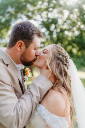 Intimate wedding kiss captured in golden sunlight with natural outdoor backdrop.