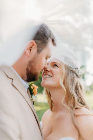 Tender moment between newlyweds under veil with soft natural lighting.