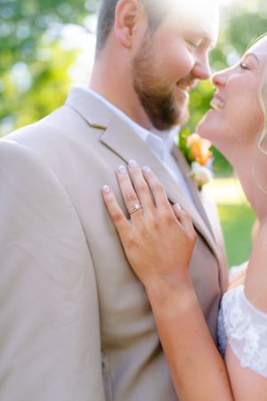 Bride shows off engagement ring while embracing in romantic outdoor portrait.
