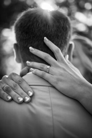 Close-up of hands with wedding rings embracing in black and white photography.