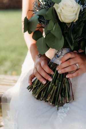 Close-up of hands holding an elegant white rose bouquet with eucalyptus leaves, showing a sparkling engagement ring.