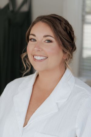 Getting ready portrait in white robe with elegant bridal makeup and updo hairstyle.