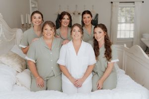 Wedding party in matching robes poses together on white bed during getting ready session.