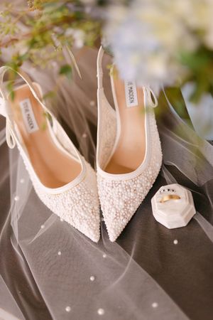 Elegant white bridal shoes with delicate pearl embellishments displayed against a dark background.