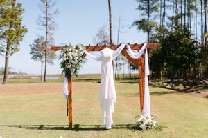 A panoramic view of an outdoor wedding ceremony setup with white fabric draping and wooden posts on a grassy hillside.
