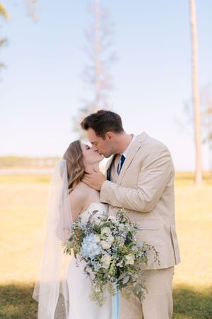 Romantic wedding couple shares intimate kisses in a garden setting with a beautiful floral bouquet.