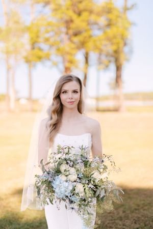 A bride poses with an elegant blue and white bouquet against a backdrop of yellow fall foliage.