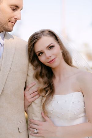 Bride in white gown and groom in beige suit share tender moments during their wedding photoshoot.