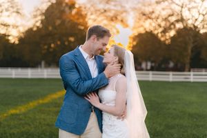 A romantic sunset wedding photo of a couple sharing a kiss in a grassy field.