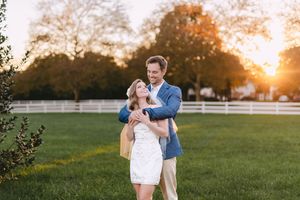 Newlyweds embrace in a grassy field during golden hour sunset creating a romantic silhouette.