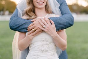 Close-up shot of an engagement ring with a lace dress and blue suit in soft natural lighting.