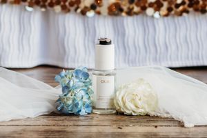 Wedding styling details featuring a white bottle, hydrangeas and rose on wooden surface.