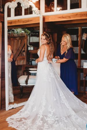 Wedding dress preparation scene in a rustic wooden interior with ornate mirror.