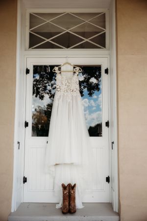 A white wedding dress hangs on a classic white door with cowboy boots placed beneath.