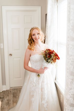 Wedding portrait of bride in white lace gown holding autumn-colored bouquet.