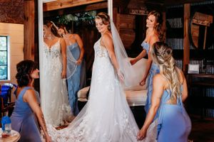 Wedding dress fitting moment with attendants in blue dresses helping with final adjustments.