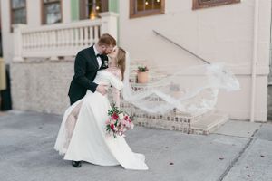 A romantic wedding couple shares a kiss on a white porch as the bride's veil flows dramatically in the breeze.