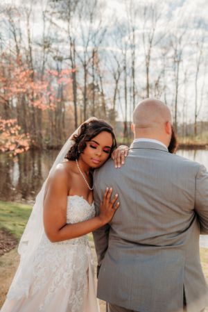 Intimate wedding photo capturing tender moment between newlyweds by lake.