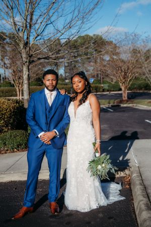 Newlyweds in elegant blue suit and lace wedding gown pose together outdoors.