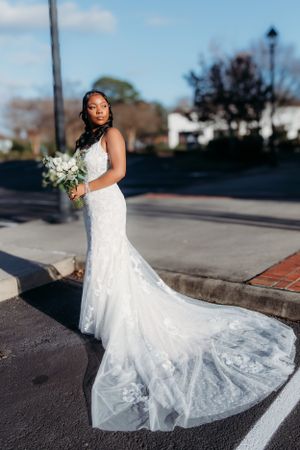 Bride in stunning lace mermaid wedding gown with long train poses outdoors.